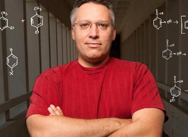 Man in Red Shirt against a chalkboard with chemical structures