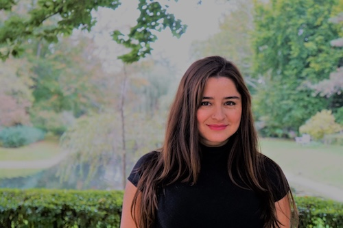 Woman in a black shirt standing in front of some greenery outdoors, smiling at the camera