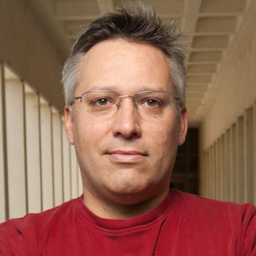 Photo of a man in a red shirt wearing glasses smiling at the camera