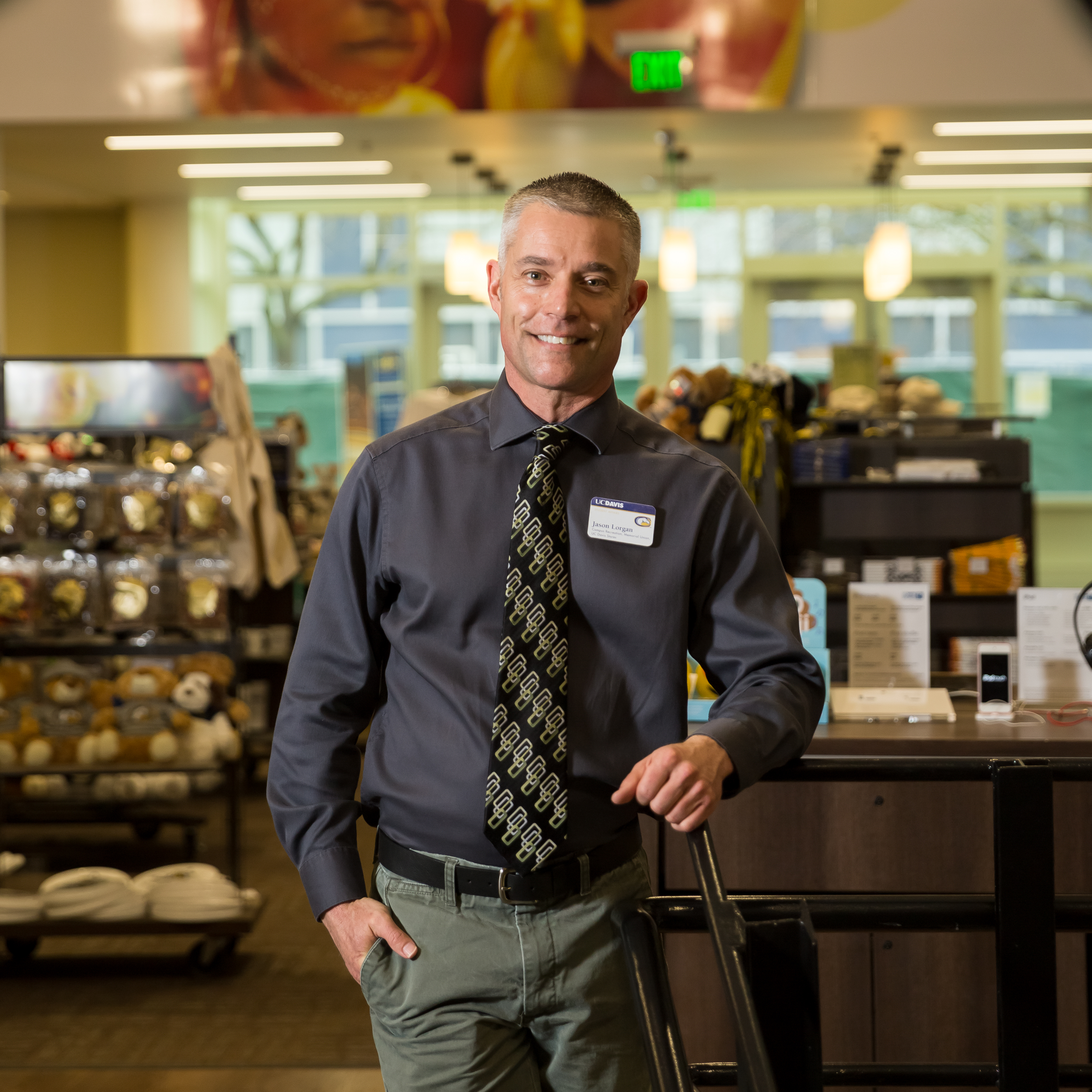 professional photo of a man in a dark button down shirt and striped tie standing in a campus bookstore 